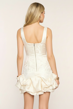 Ivory floral jacquard bodycon mini dress straight back view – back zipper closure structured ruffle hem with gold bracelets on blonde European model